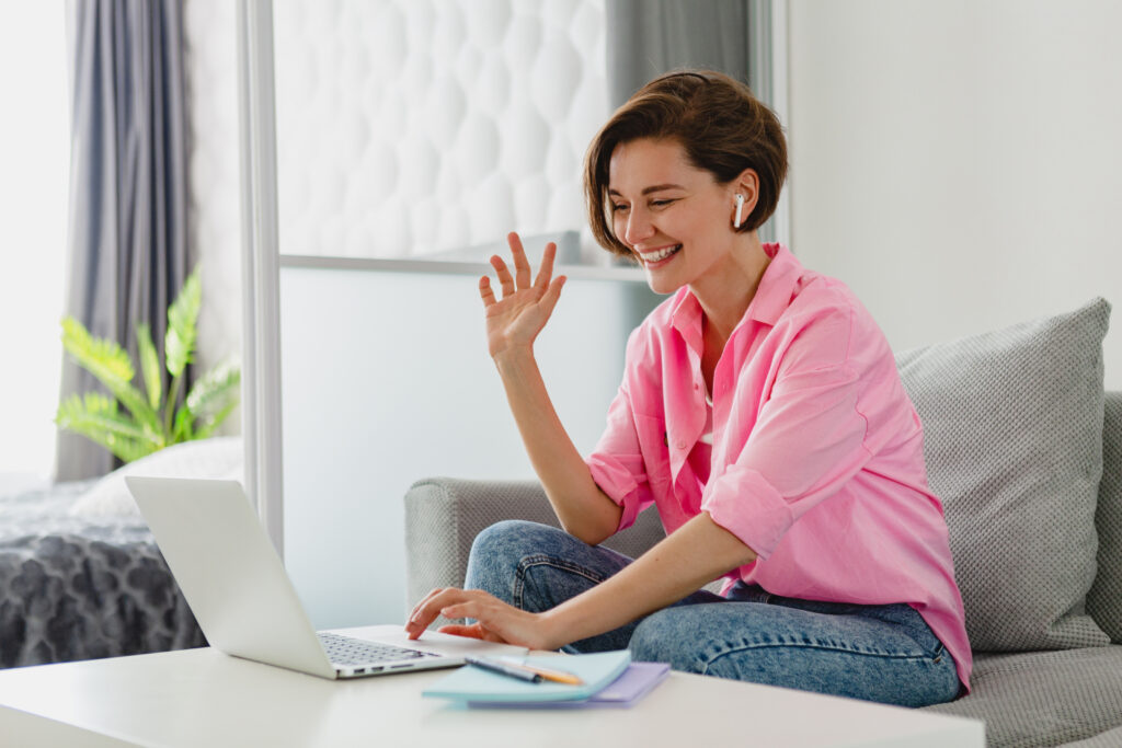Woman in pink blouse, following private Dutch lessons online, sitting on the couch in her living room.