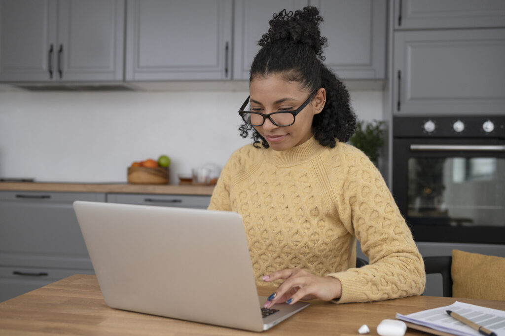Woman in yellow sweater behind her laptop, following the Dutch A2 exam training.