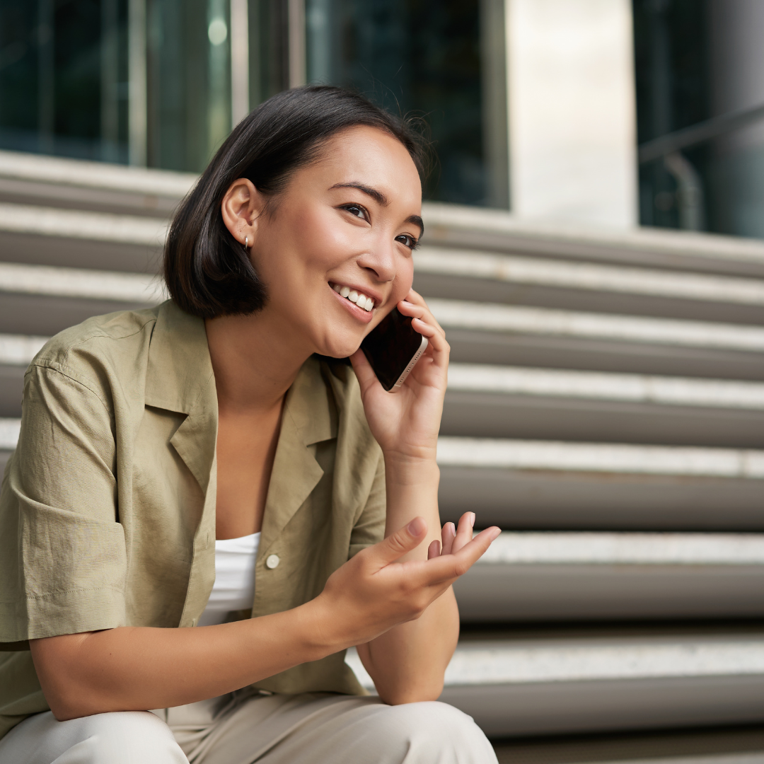 Young woman sitting on the stairs making a phone call to Dutch Ready to discuss her questions about an NT2 Dutch course.