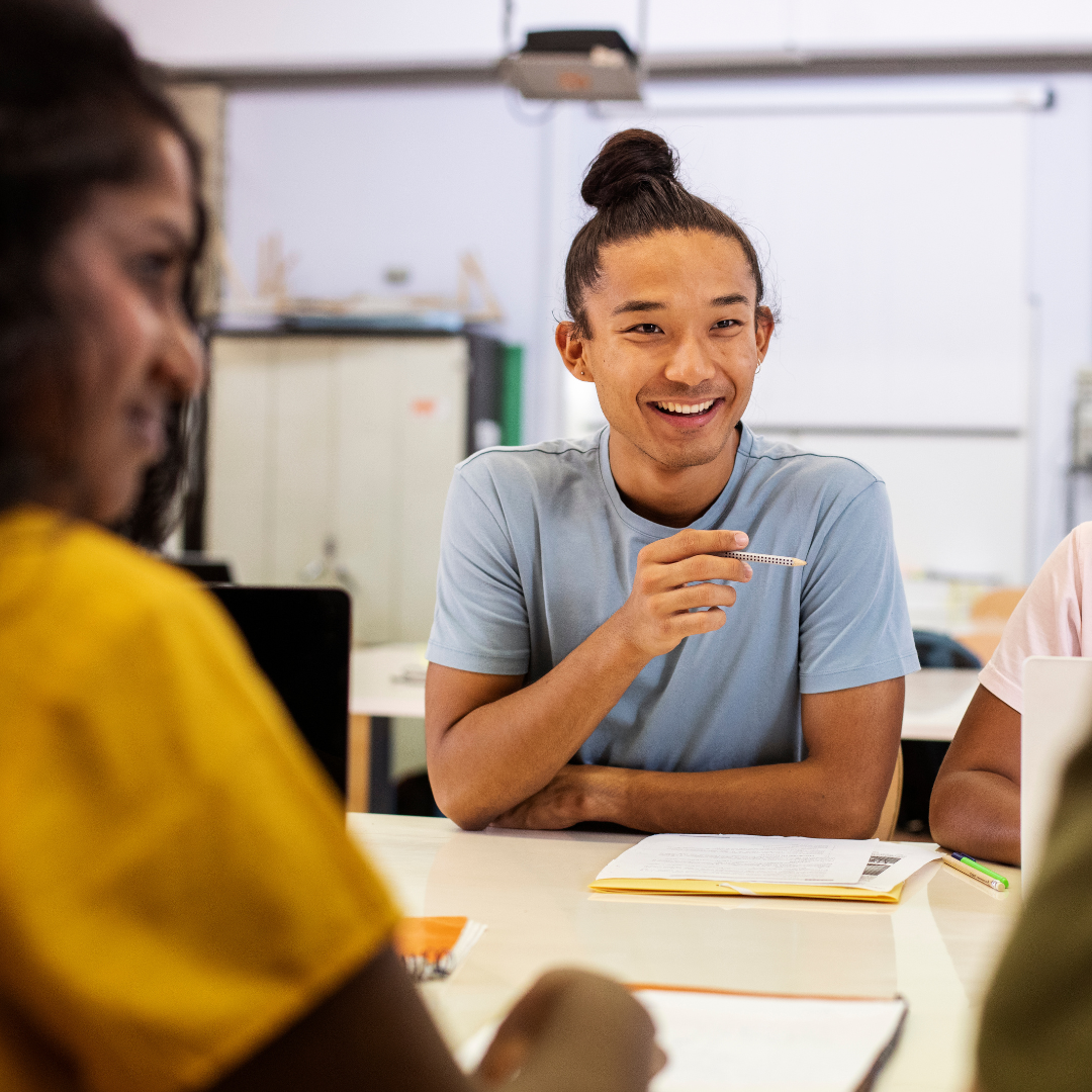 An enthusiastic student conversing with his Dutch tutor, who is seated opposite him. A fellow student is also seated at the table.