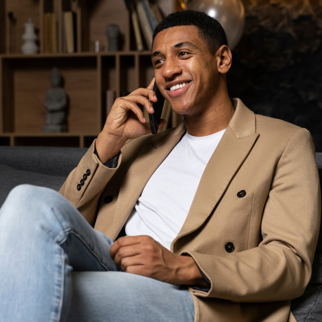 Young man in jeans and a jacket talking on the phone about Dutch lessons in Haarlem. He is sitting relaxed in an office chair.