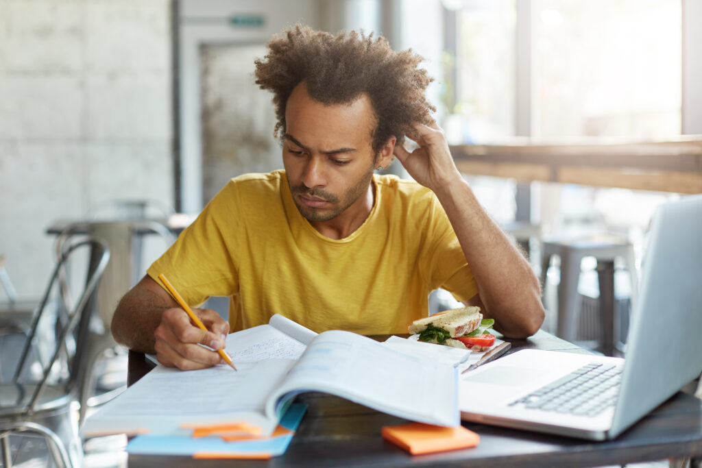 Male student in yellow T-shirt who pensively studies Dutch grammar in his book.