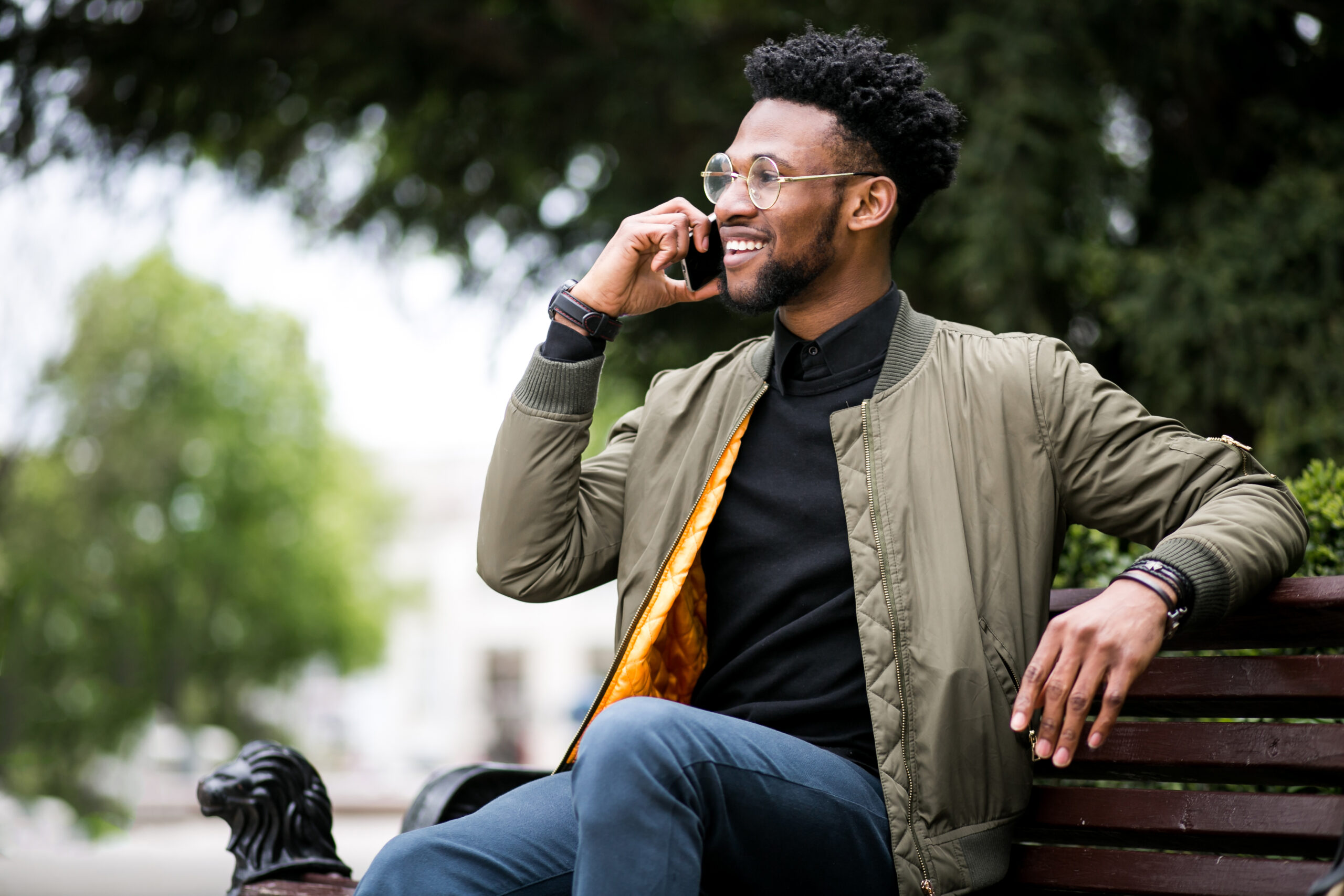 Young man sitting outside on a bench, talking on his mobile phone about Dutch conversation lessons.