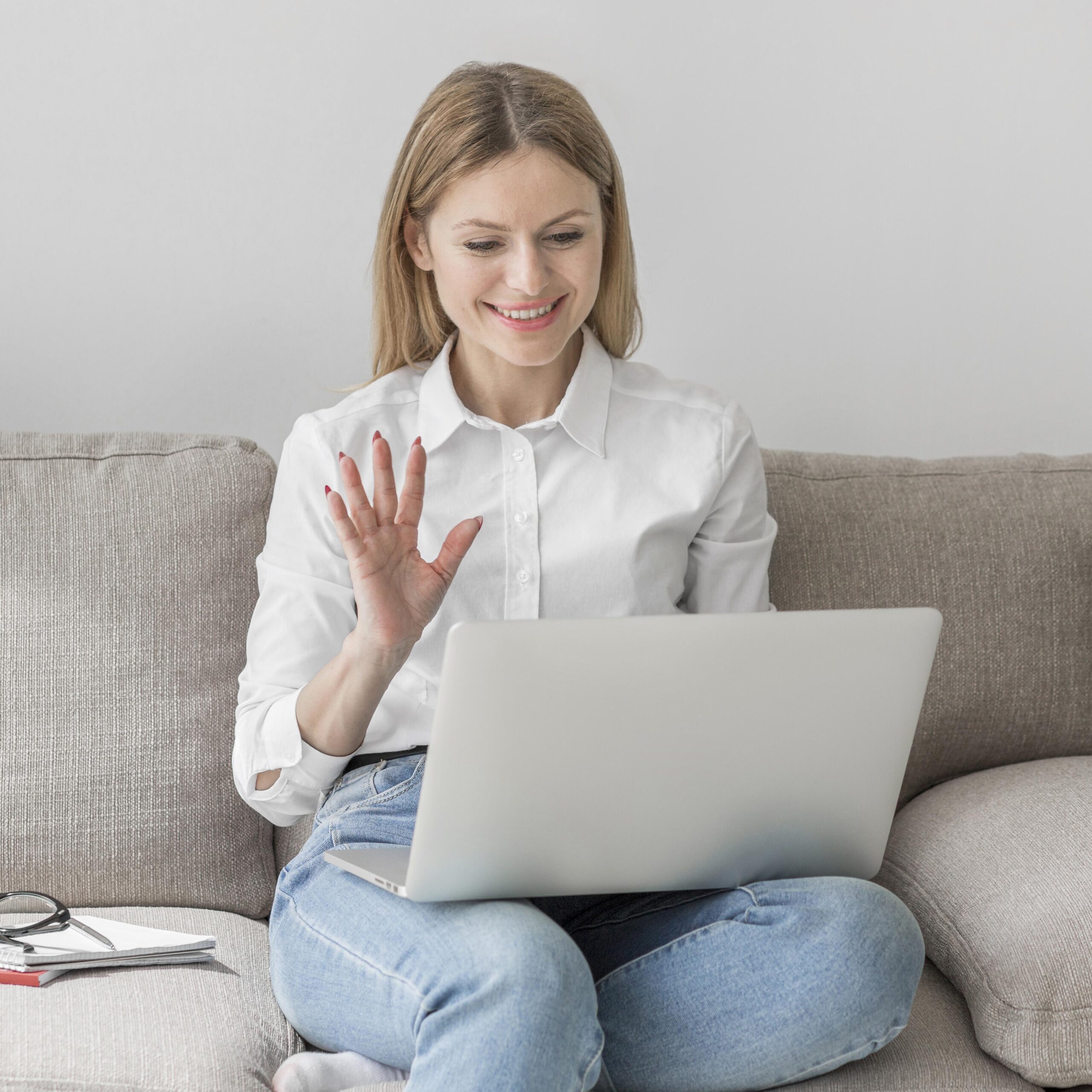 Female student sitting on the couch with her laptop, waving to her Dutch tutor at the beginning of their test lesson.