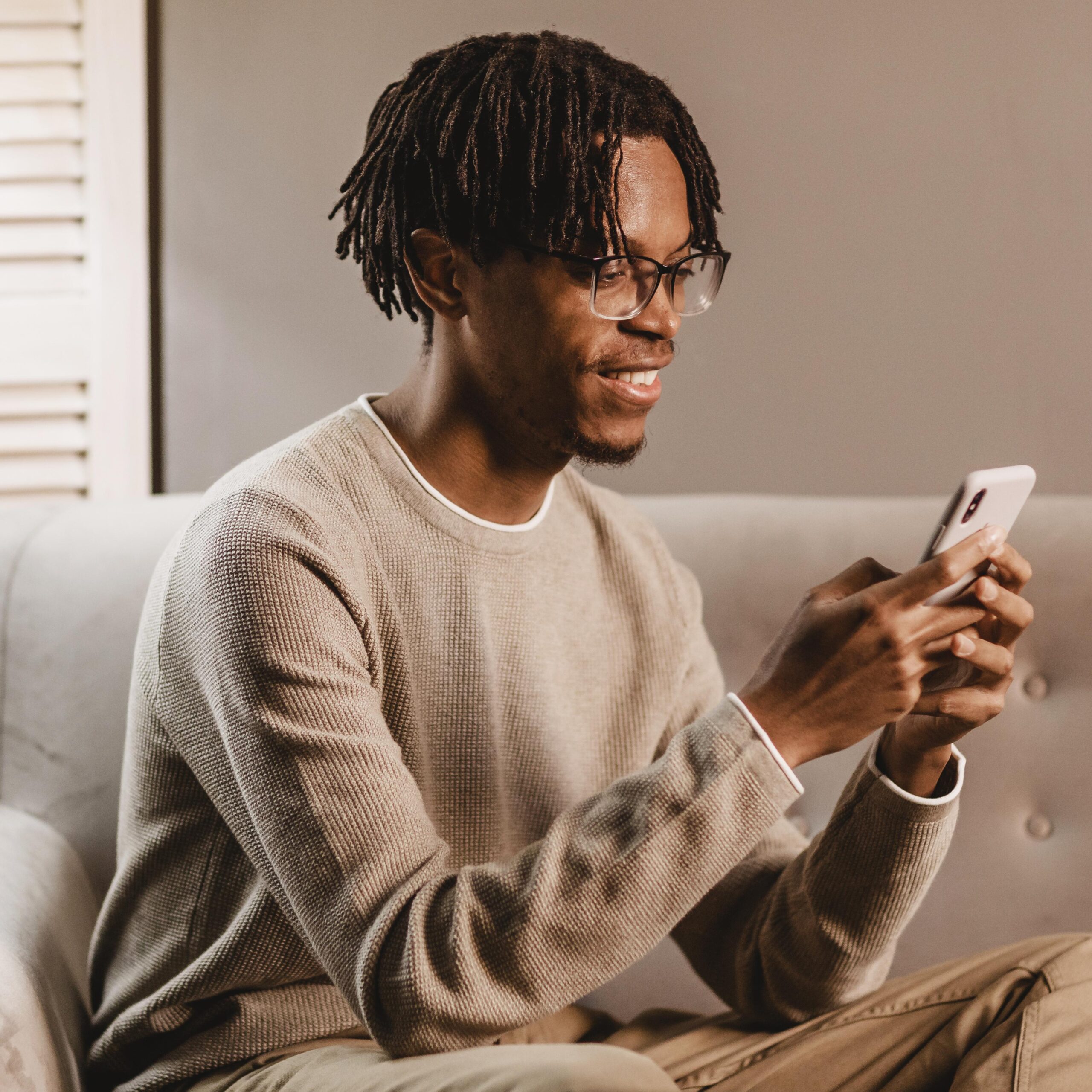 Young man with glasses, sitting on his couch, while he takes a phone call about short Dutch conversations.