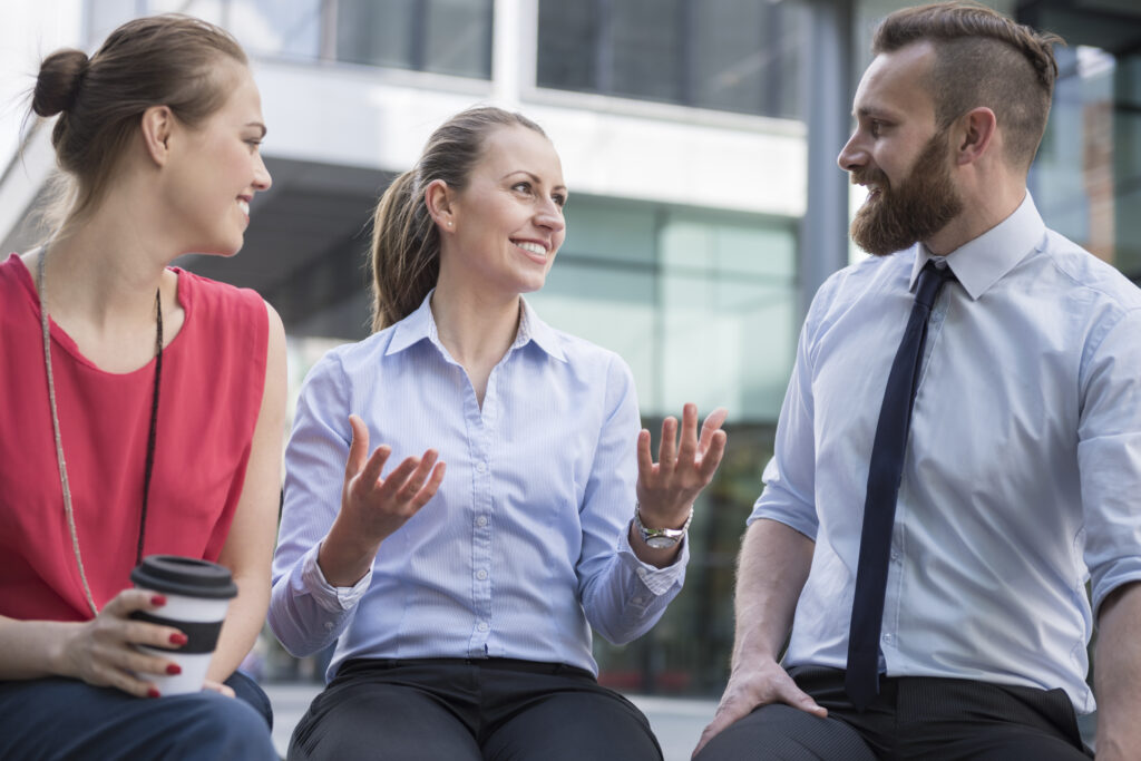 Young businesswoman who is starting to overcome her fear of speaking Dutch, and holds a friendly conversation with 2 colleagues outside.