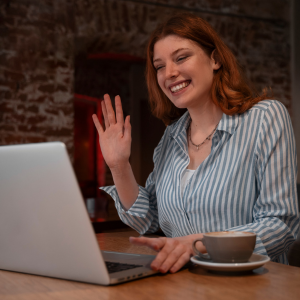 Casually dressed business woman following online private inburgering lessons, waving to her tutor at the laptop screen.