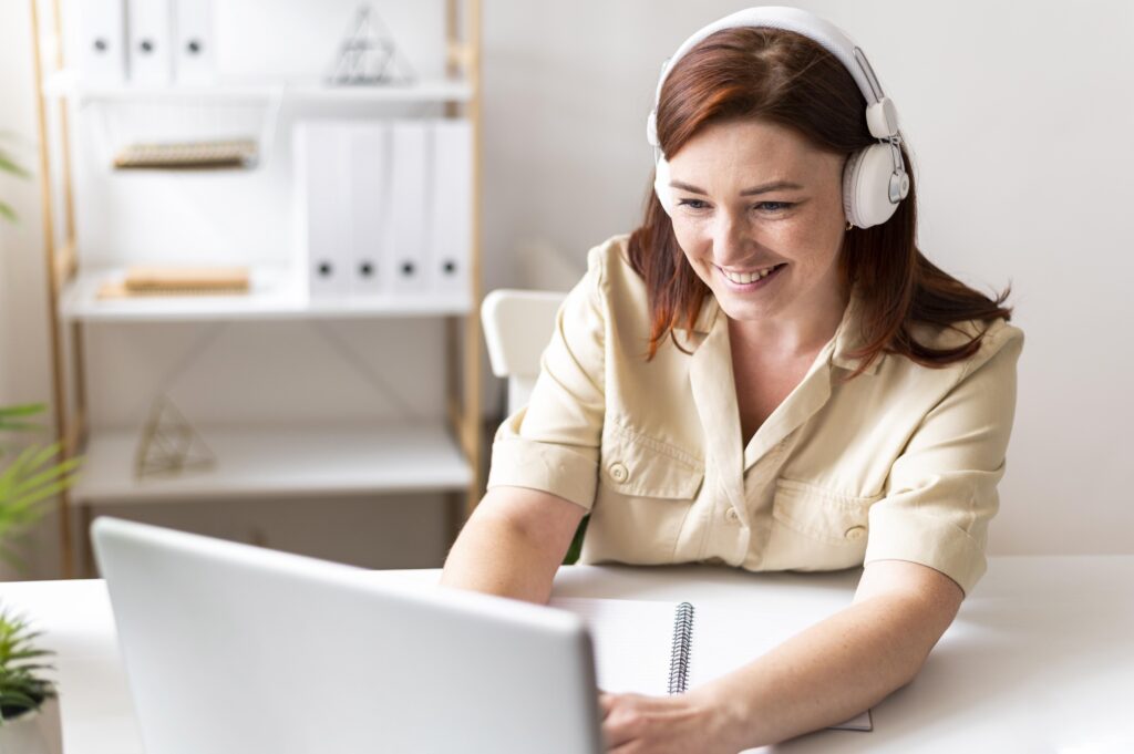 A young female expat wearing headphones, sitting behind her laptop while studying to pass her Dutch exams with Dutch Ready Academy's self-study platform.